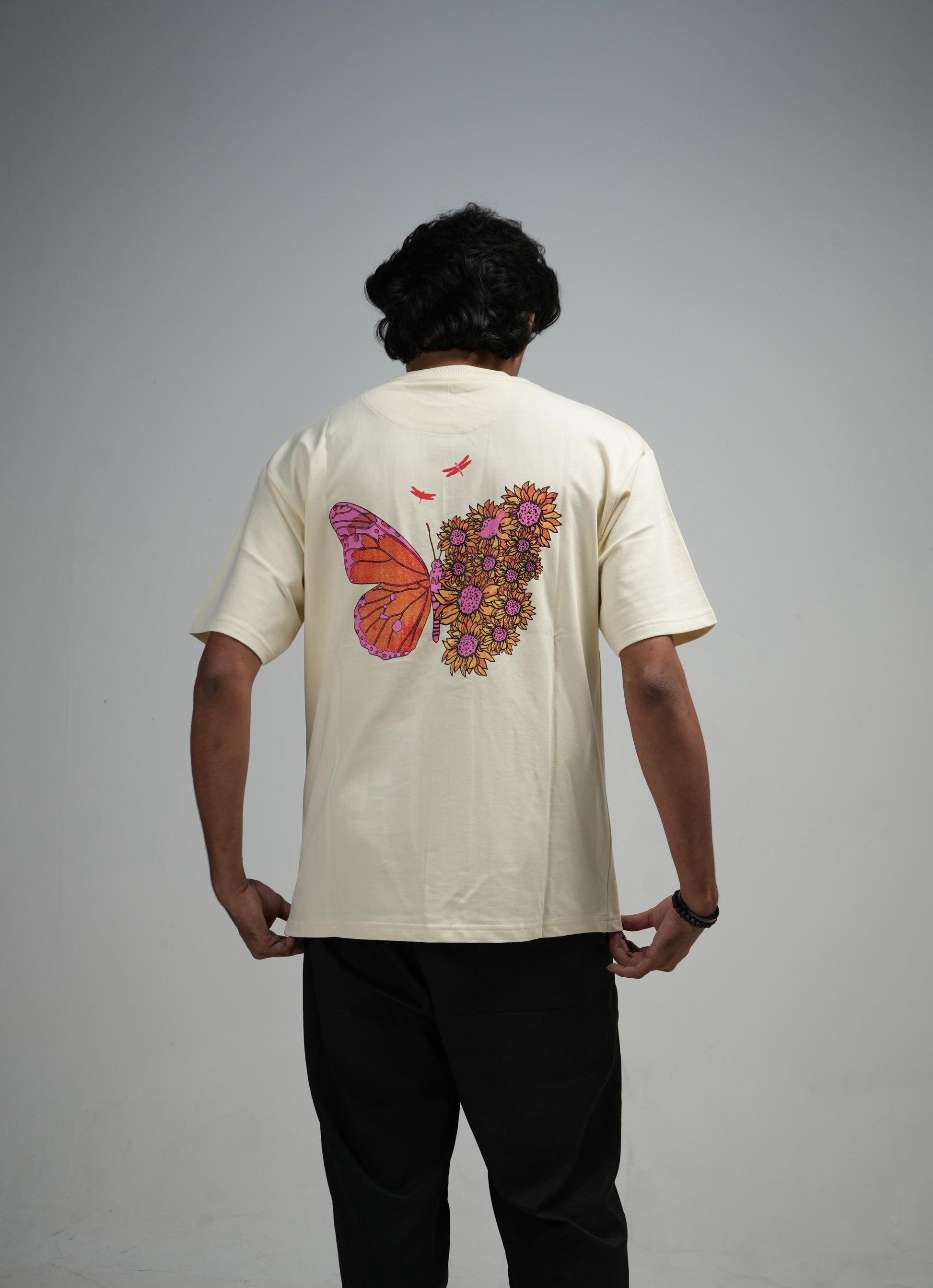 Person wearing a beige shirt with a butterfly design on the back against a plain background
